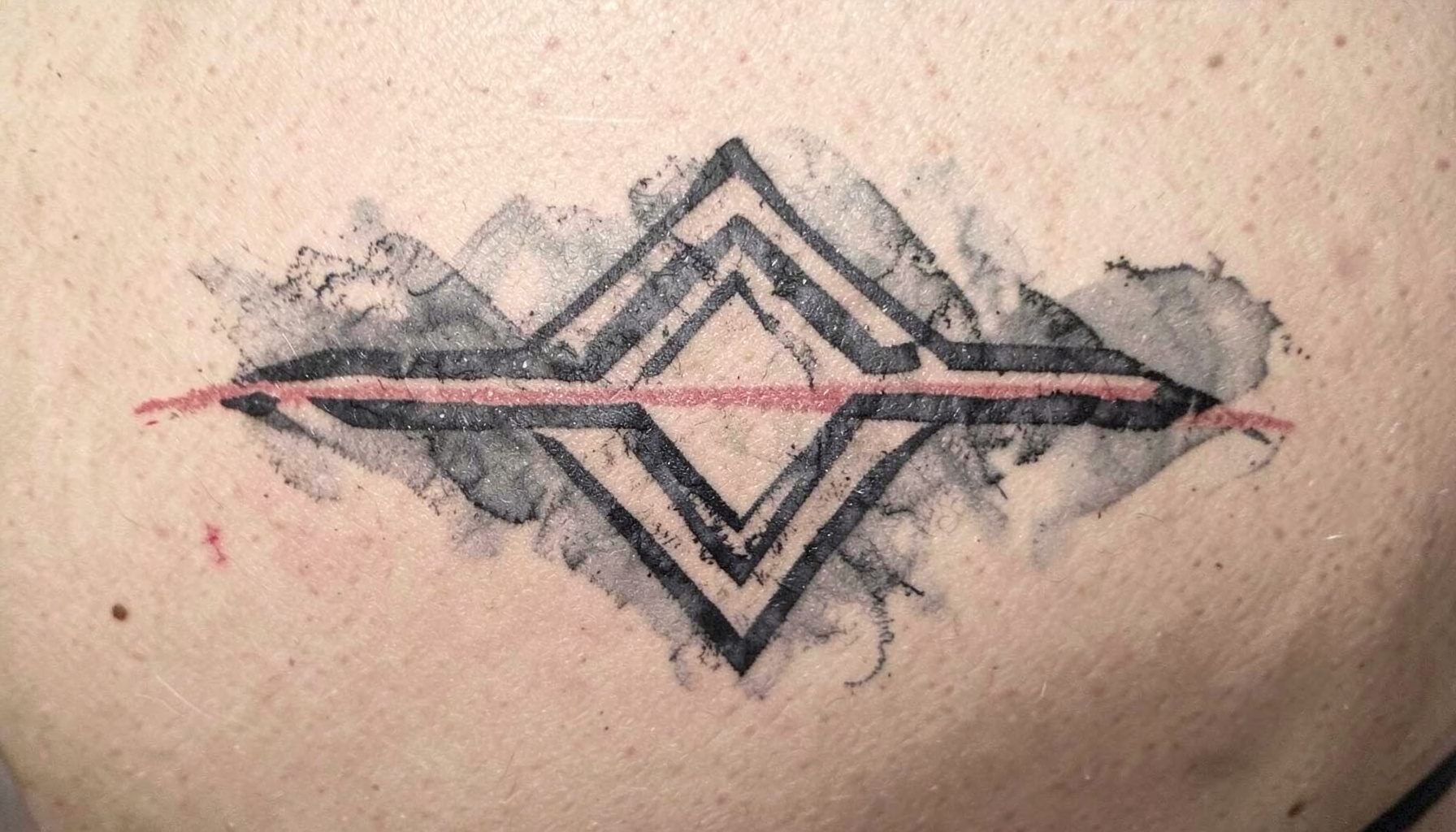 A completed Sak Yant geometric design on skin, bold charcoal linework with soft grey shading against a neutral background.